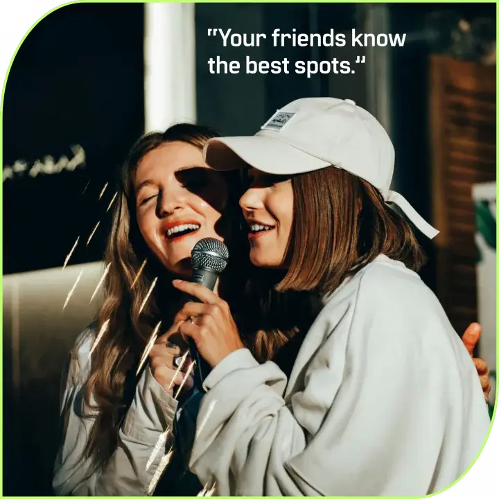 2B LOCAL app: Two women smiling and hugging on stage, one holding a microphone between them.